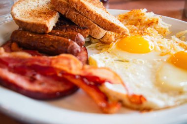 Kahvaltıda yumurta, domuz pastırması, tost ve sosis yakın plan çekilmiş.