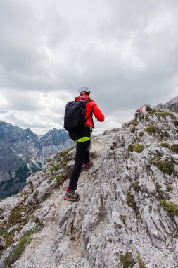 Donanımlı bir yürüyüşçü Bulutlu bir günde Alp yüksek irtifasında Rocky yolunda yürüyor.