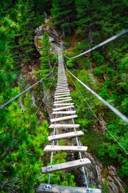 Tırmanışçılar için Ferrata üzerinden Avusturya Stüdyolarının tahta Plank Çelik Kablolarından yapılmış doğa manzarasına uzanan Maceracı Asma Köprüsü