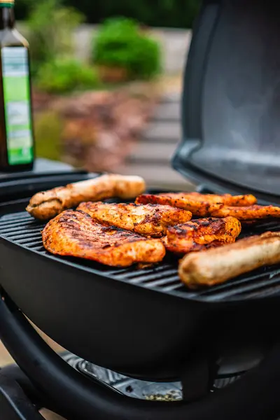 stock image Delicious Chicken Steaks and Sausages Getting Grilled on a Hot Black Grill Grate off a Small Electrical Garden Grill