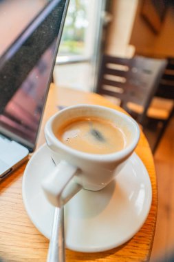 Çalışma sırasında kafein yoluyla odaklanmak için bilgisayar not defterinin yanında bir kahvecide Espresso bardağındaki siyah kahve.