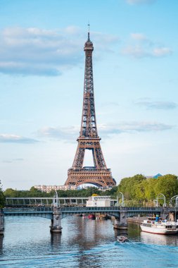 Eyfel Kulesi Gökyüzüne yükseliyor. Tekneler Seine Nehri 'nde bir köprünün altında ilerliyor.