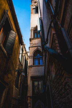 İtalya, Venedik 'teki yüksek tarihi binalar tarafından çerçevelenmiş dar sokakları keşfedin. Sahne çarpıcı bir mimari, mavi gökyüzü yakalıyor ve kentsel keşif titreşimleri sunuyor..