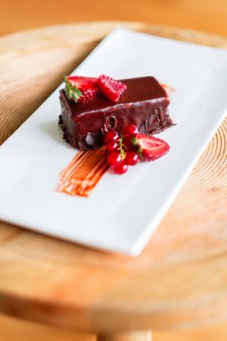 Taze böğürtlenlerle süslenmiş bir gurme çikolatalı tatlı. Zarif bir beyaz tabakta sunulan bu ikram, zengin tatlar ve zarif bir sunumla lüks bir yemek deneyimi sunuyor..