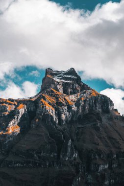 Pofuduk mavi gökyüzüne uzanan engebeli bir dağın çarpıcı manzarası, kabarık bulutlarla çevrili, doğanın el değmemiş güzelliğinin somutlaştırıcı vahşi doğası ve sükuneti..