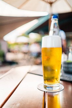 Soğuk bir bira, dışarıdaki ahşap bir masada oturup rahatlatıcı bir atmosfer yakalıyor. Boş zaman, yaz ve sosyal etkinlikler için ideal..