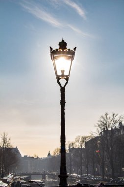 Zarif bir sokak lambası, berrak mavi bir gökyüzü altında sakin bir caddeyi aydınlatıyor. Sabahları sakin bir şehirde klasik Avrupa mimarisi ve şehir sakinliği sergiliyor..