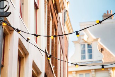 Captivating urban landscape showcasing string lights hanging between historical buildings. The warm glow creates a welcoming and festive atmosphere against the blue sky. clipart