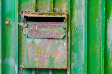 Paslı, eski, yeşil metal bir posta kutusunun detaylı bir görüntüsü, eski bir endüstriyel görünüm sergiliyor. Doku, şehir sahnesine karakter ve geçmiş ekler..
