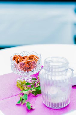 Crystal dish with salted pretzels on a purple napkin, complemented by green foliage, creates a stylish and contemporary culinary display in a bright and elegant setting. clipart