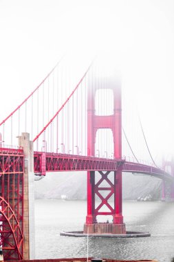 Altın Kapı Köprüsü yoğun sisin içinden San Francisco Körfezi 'nin sakin sularına karşı canlı kırmızı çelik yapısını sergileyerek çarpıcı bir mimari başyapıt yarattı..