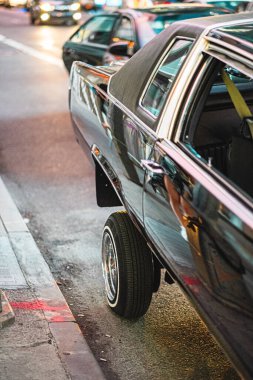 Yükseltilmiş tekerli klasik siyah bir araba gece kalabalık bir şehir caddesinde park edilmiş, hareketli şehir ışıklarını ve gece hayatının dinamik atmosferini vurguluyor..