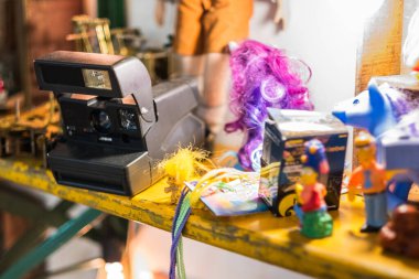 A vintage Polaroid camera sits alongside an assortment of colorful toys and knick-knacks on a yellow shelf, creating a nostalgic and playful atmosphere. clipart