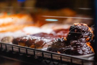 Close-up view of chocolate glazed donuts in a bakery display, showing delicious tempting flavors. The dim lighting enhances the indulgent and inviting atmosphere for sweet treat enthusiasts clipart