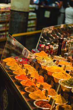 Bir marketin tezgahında renkli baharatlar sergileniyor, çeşitli aromalar ve dokular sergileniyor. Baharatların zengin renkleri şehir pazarında canlı bir sahne yaratıyor..