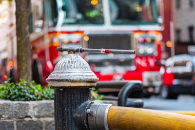 A fire hydrant with hose valve in focus and a blurred fire truck in the background, depicting urban emergency services and essential infrastructure on a bustling city street. clipart