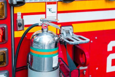 İtfaiye aracındaki yangın söndürücüye yakın plan güvenlik ekipmanlarını ön plana çıkarıyor. Parlak yüzey ve canlı kırmızı ve sarı aksanlar acil duruma hazırlık ve profesyonelliği vurguluyor..