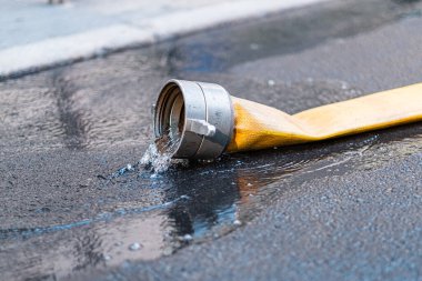 Close-up of water flowing from a yellow fire hose onto a wet street surface, illustrating firefighting and emergency response equipment in urban settings. clipart