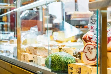 Taze İtalyan peynirleri, etleri ve sebzeleri olan bir şarküteri tezgahının yakın çekimi. Fiyat etiketleri otantik pazar ayarlarını gösteriyor. Bir İtalyan şarküterisinin canlı ve davetkar atmosferini yakalıyor.