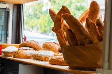 Taze fırınlanmış ekmek somunları ve baget ekmeği sergilenen sıcak bir fırın, güneşli bir pencerenin yanında güzelce düzenlenmiş, zanaatkar pişirmenin özünü yakalıyor..