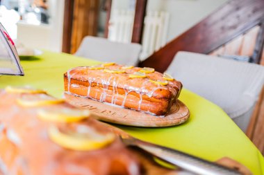 Ağız sulandıran limonlu kek, ahşap bir tabağın üzerinde oturur, güzel bir şekilde hazırlanmış, rahat bir mutfakta. Doğal ışık, tatlı meraklıları ve çay saatleri için ideal olan kekin lezzetini vurgular..