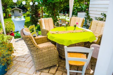 Canlı yeşil bir masa örtüsüyle hasır sandalyelerin olduğu rahat bir bahçe sahnesi. Yaz toplantıları, brunch 'lar ya da güneşin altındaki yemyeşil bir bahçede dinlenmek için idealdir..