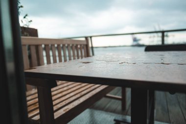 Tahta bir açık masa ve bir balkonda yağmur damlaları olan bank bulutlu bir günde liman manzarası sağlıyor. Doğada huzur ve rahatlama temaları için idealdir..