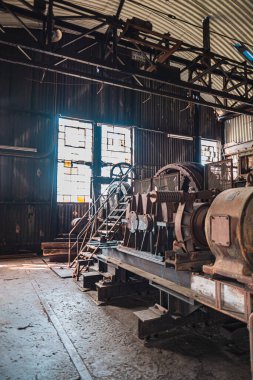 Eski makinelerin ve çelik kirişlerin gösterileceği klasik bir endüstriyel atölyenin iç görüntüsü, doğal ışıkla aydınlanarak, tarihi bir mühendislik mirası hissi uyandırıyor..