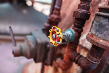 Detailed image highlighting a weathered valve with a colorful wheel amidst a backdrop of rusted pipes, depicting an industrial atmosphere and a vintage mechanical aesthetic. clipart