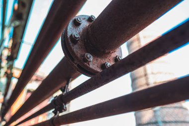 Endüstriyel ortamda cıvata ve fındıklı paslı metal boru hatlarının yakın plan görüntüsü, eski dokusunu gösteriyor. Görüntü endüstriyel ekipmanların özünü ve yaşlanmanın etkilerini yakalıyor..