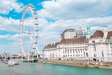 Güzel bir panoramik manzara, Londra Gözü 'nü ve Thames nehri boyunca tarihi mimariyi gözler önüne seriyor. Parlak mavi gökyüzü ve tüylü beyaz bulutlar üzerine kurulmuş..