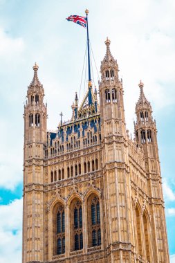 Parlak mavi bir gökyüzüne kurulmuş İngiliz bayrağıyla süslenmiş görkemli Gotik mimarisi. Bu resim Londra 'nın zengin kültürel mirasını ve tarihsel zarafetini sergiliyor.