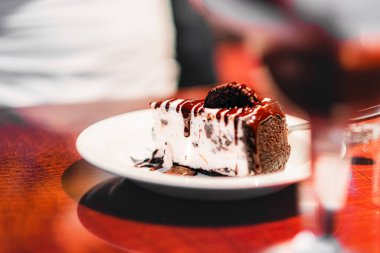 Kremayla kaplı ağız sulandıran bir dilim çikolatalı pasta ve beyaz bir tabakta Oreo 'ya benzer bir kurabiye sunulur. Sıcak bir kafe atmosferinin sıcaklığını yakalar..