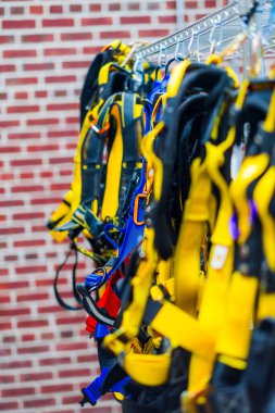 Collection of safety harnesses hang neatly in a warehouse, highlighting industrial safety and preparation. The brick backdrop adds to the professional setting and focus on protective equipment clipart