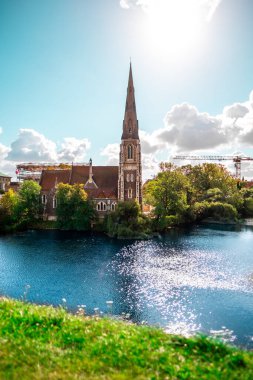 Güzel, tarihi bir kilise, yemyeşil sularla çevrili parıldayan bir nehrin yanında duruyor. Parlak güneş manzarayı aydınlatır çarpıcı mimariyi ve sakin açık hava atmosferini güçlendirir..
