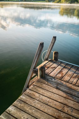 Huzurlu sulara çıkan bir merdivenle sakin bir rıhtım manzarası. Sakin göl, huzurlu çevreyi yansıtır. Uyumlu ve sakin bir atmosfer yaratır..