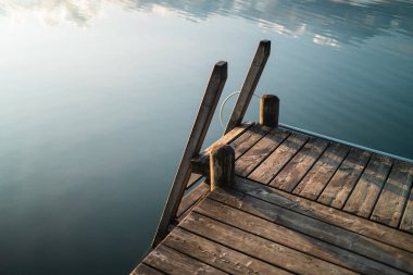Sakin bir göl ortamında, sakin suların üzerine uzanan ahşap bir rıhtım sabah ışığı altında yakalanır. Bu huzurlu sahne huzur, yansıma ve doğanın güzelliğini çağrıştırıyor..