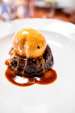 Bir kepçe vanilyalı dondurmayla kaplanmış, bol soslu nefis çikolatalı tatlı. Samimi bir yemek atmosferinde yakalanmış, gurme yemek sunumları için mükemmel..