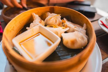 Soya soslu bambu sepetinde servis edilen buharda pişirilmiş hamur köftelerinin yakın çekimi. Geleneksel Asya mutfağını yakalar ve otantik bir yemek deneyimi için mükemmel bir Dim Sum tabağı sunar.
