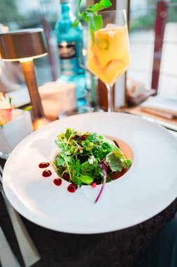 Taze, ferahlatıcı bir narenciye kokteyli ile eşleştirilmiş salata, sofistike bir restoran ortamında güzel sunulmuş, gurme mutfağından zevk almak için mükemmel bir yemek deneyimi.