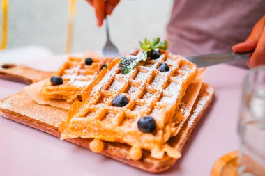 Ağız sulandıran Belçika waffleları yaban mersinleri, pudra şekeri ve servis tahtasında nane şekeri ile süslenir. Kahvaltı ya da kahvaltı için mükemmel. Şımarık bir sabah yemeğinin özünü yakalar..