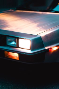 Klasik tasarımının altını çizerek, klasik bir arabanın alacakaranlıkta aydınlatılmış farının yakın çekimi. Metalik yüzeyde hafif yansımalar, arabanın stil ve zamansız cazibesini vurguluyor..