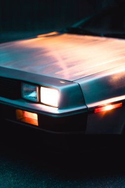 Modası geçmiş bir arabanın farının karamsar yansımaları ve ışıklandırmasıyla yakın çekimi. Görüntü klasik otomobil tasarımını vurguluyor, nostalji ve furüristik stili çağrıştırıyor