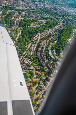 Manzaralı bir hava perspektifi, aydınlık gün ışığında hafif bir uçağın penceresinden bakıldığında bol yeşillikle çevrili canlı bir yerleşim bölgesini gösteriyor..