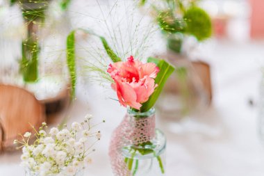 Yeşil yapraklar ve çiçekli süslemelerle tamamlanmış camdan bir vazoda sergilenen pembe karanfil hoş ve canlı bir ortam sunuyor..