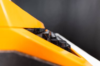 Pürüzsüz, karanlık bir arkaplan karşısında sunulan dokulu siyah düğmeleri içeren turuncu bir cihazın canlı detaylı görüntüsü, teknoloji ve soyut bileşim üzerine bir odak hissi veriyor..