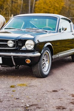 Çakıl taşlı bir yolda krom detaylara sahip klasik siyah bir araba, zarif tasarımını sergiliyor ve doğal ortamlardaki klasik otomobillerin güzelliğini vurguluyor..