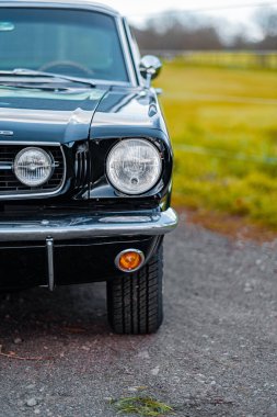 Klasik siyah bir arabanın ön kısmının parlak krom farlarını, zarif vintage detaylarını ve kırsal bir arka plandaki eşsiz karakterini gösteren yakın plan görüntüsü..
