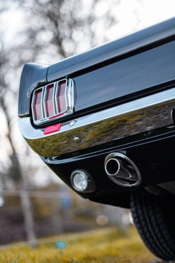 Klasik bir arabanın arka kısmının odaklanmış görüntüsü arka farlarını, krom tamponunu ve egzoz sistemini vurguluyor, klasik tasarım ve cilalı işçiliği vurguluyor..