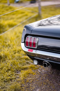 Eski bir otomobilin arka lambasının ve tamponunun krom ve klasik tasarımını gösteren ayrıntılı fotoğraf, açık havada bulanık doğal arka plan ve canlı çimlerle hazırlandı.